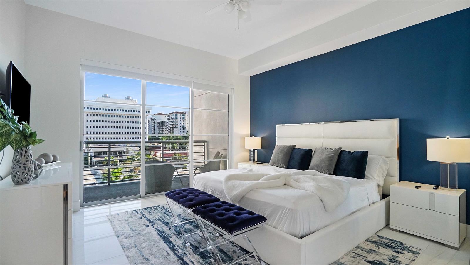 A modern bedroom features a blue accent wall, white furniture, and a balcony with city views — 155 E Boca Raton Road # 501, Boca Raton FL 33432, BOCA RATON, FL