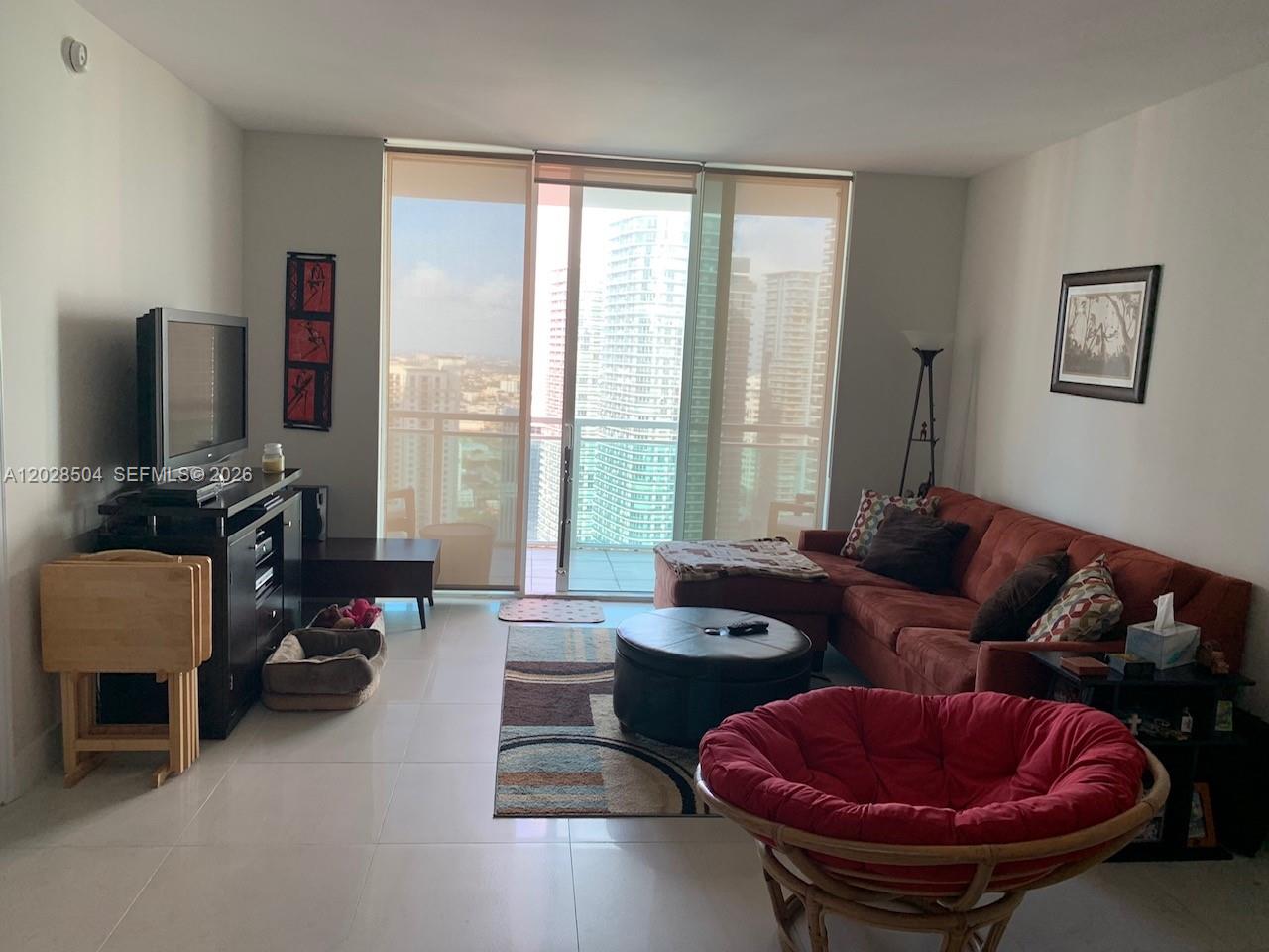 A living room features a red sectional sofa, a round chair, and floor-to-ceiling balcony windows — 951 Brickell Ave # 4005, Miami FL 33131, MIAMI, FL