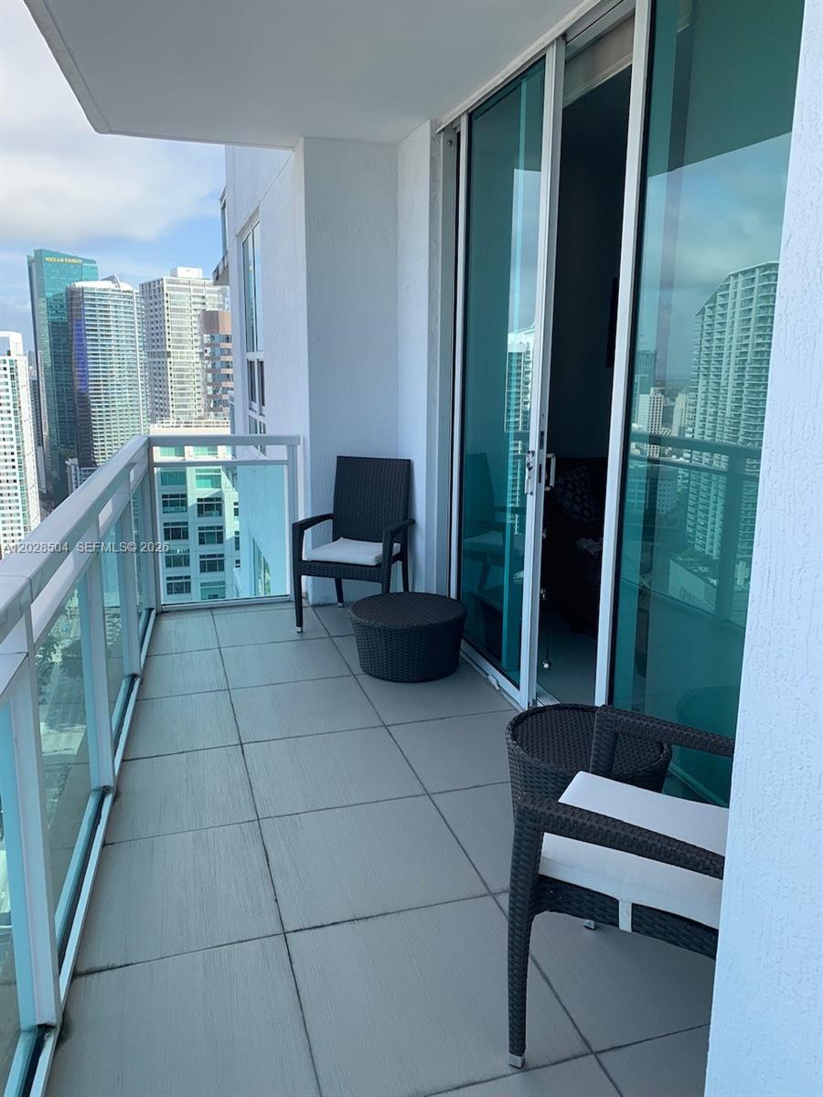 A balcony with gray tiled flooring, two wicker chairs, a small table, and city views — 951 Brickell Ave # 4005, Miami FL 33131, MIAMI, FL