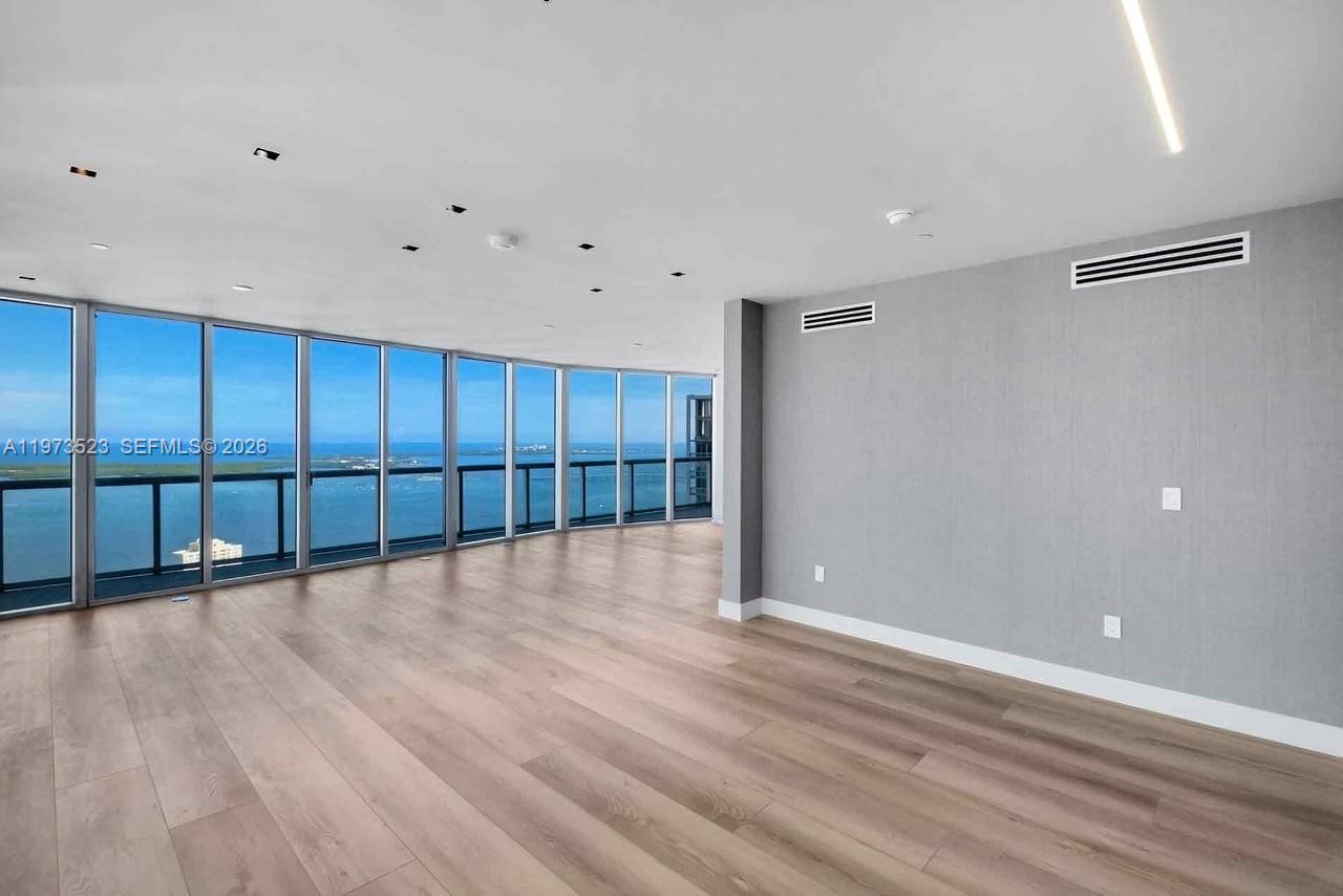 An empty room features light wood flooring, gray walls, and floor-to-ceiling windows overlooking water — 465 Brickell Ave # 5701, Miami FL 33131, MIAMI, FL