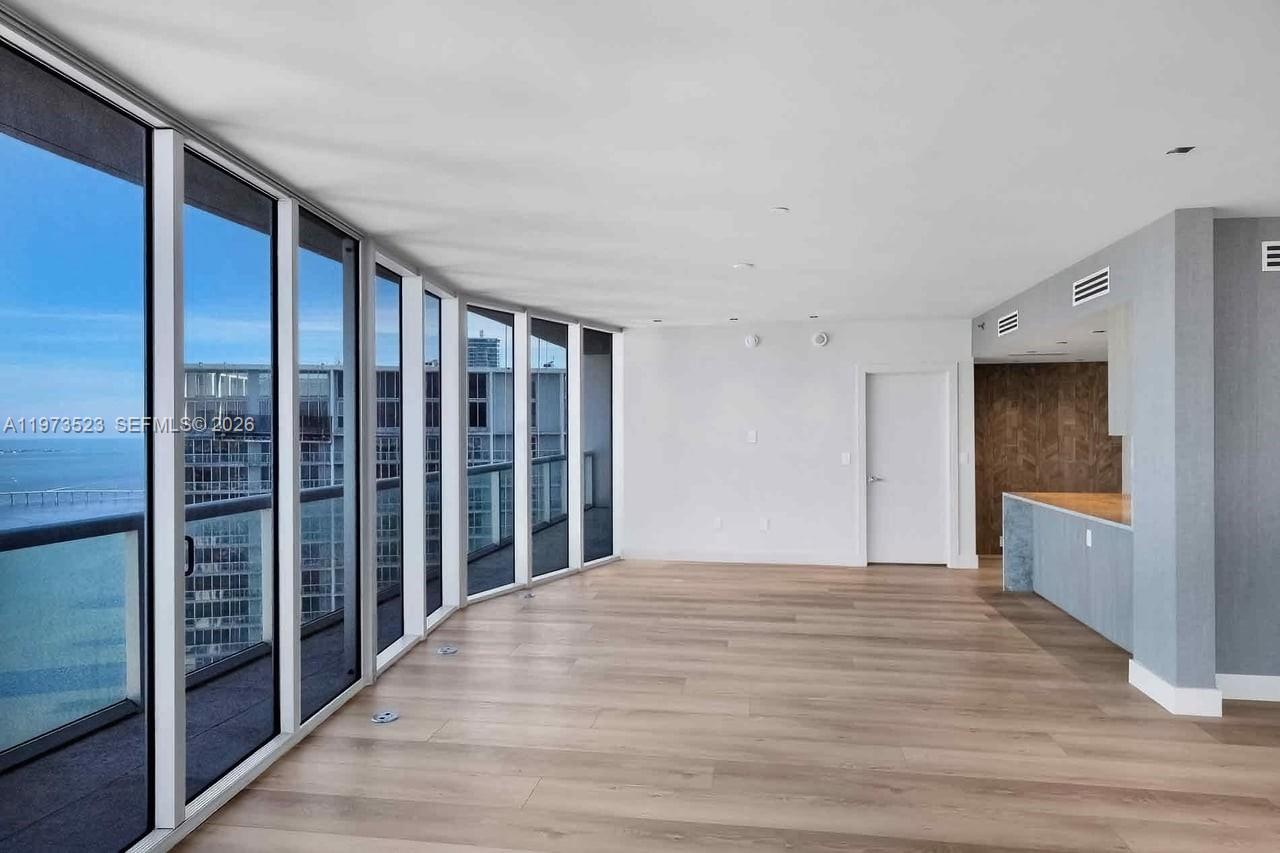 An empty living area features light wood flooring, floor-to-ceiling windows, and an adjacent kitchen — 465 Brickell Ave # 5701, Miami FL 33131, MIAMI, FL