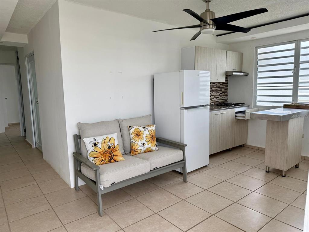 A small kitchen area features light wood cabinets, a white refrigerator, and a gray loveseat — 53 CALLE SATURNO COM SANDIN UNIT 1, VEGA BAJA, PR