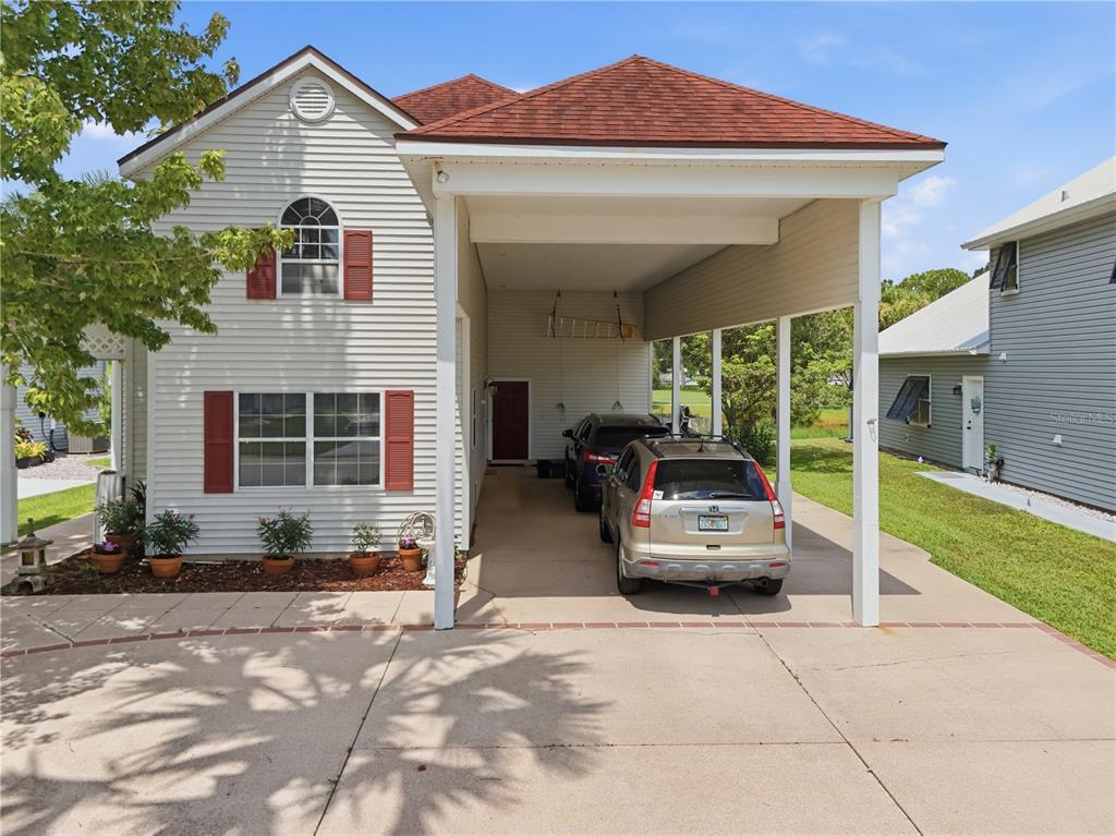 A two-story house with light siding, red shutters, and a large attached carport with two cars — 523 FAIRWAYS DRIVE UNIT 523, TITUSVILLE, FL