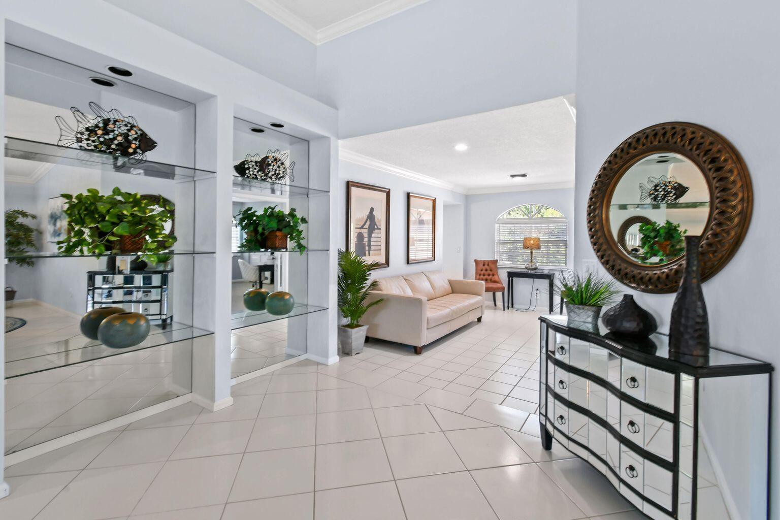 A bright foyer features mirrored display shelves, a mirrored chest, and a view into a living room — 252 Legendary Circle, Palm Beach Gardens FL 33418, PALM BEACH GARDENS, FL