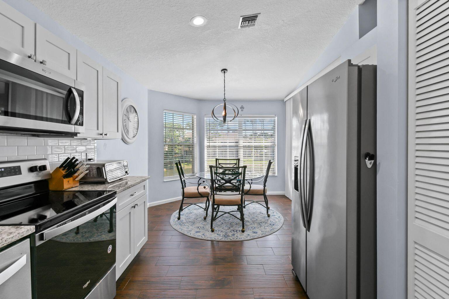 A kitchen with white cabinets, stainless steel appliances, and an adjacent dining area with windows — 252 Legendary Circle, Palm Beach Gardens FL 33418, PALM BEACH GARDENS, FL