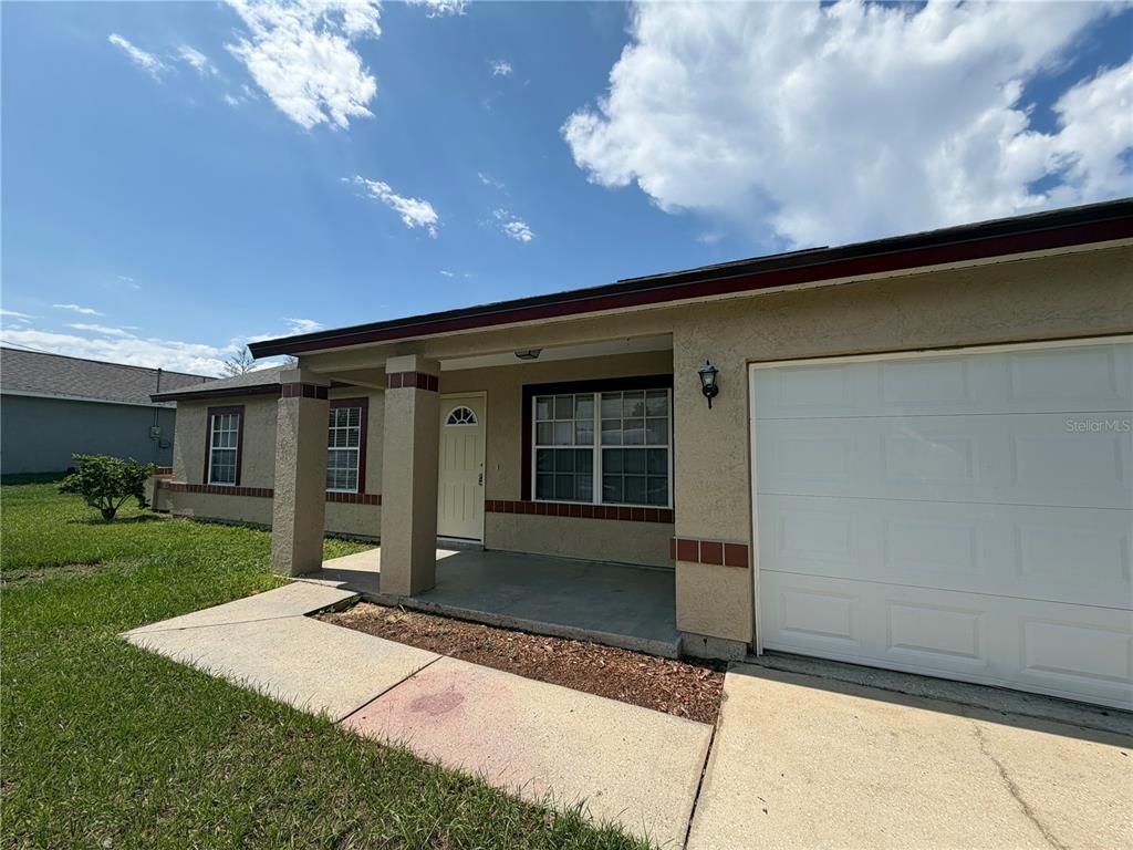 A single-story house exterior features a covered porch, a white garage door, and tan stucco — 73 OLIVE DRIVE, OCALA, FL