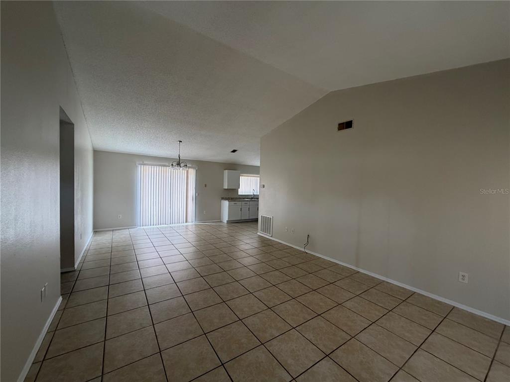 An open-concept living and dining area features beige tile flooring and a vaulted ceiling — 73 OLIVE DRIVE, OCALA, FL