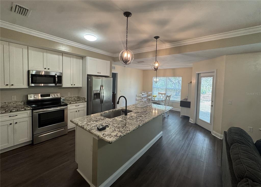 A kitchen features white cabinets, granite countertops, a center island, and stainless steel appliances — 8291 NE 118TH TERRACE, BRONSON, FL
