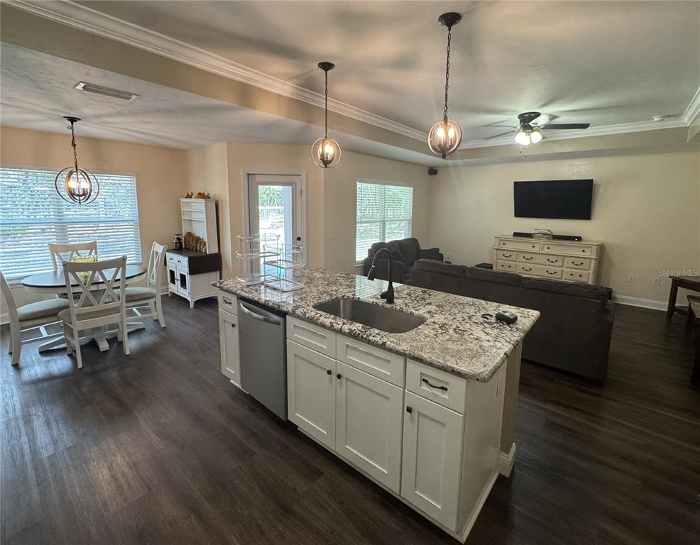 An open-concept kitchen and living area features a granite-topped island, white cabinetry, and wood flooring — 8291 NE 118TH TERRACE, BRONSON, FL