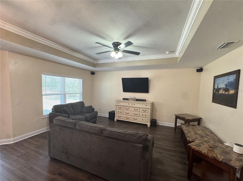A living room features a tray ceiling, dark wood-look flooring, and a wall-mounted television — 8291 NE 118TH TERRACE, BRONSON, FL