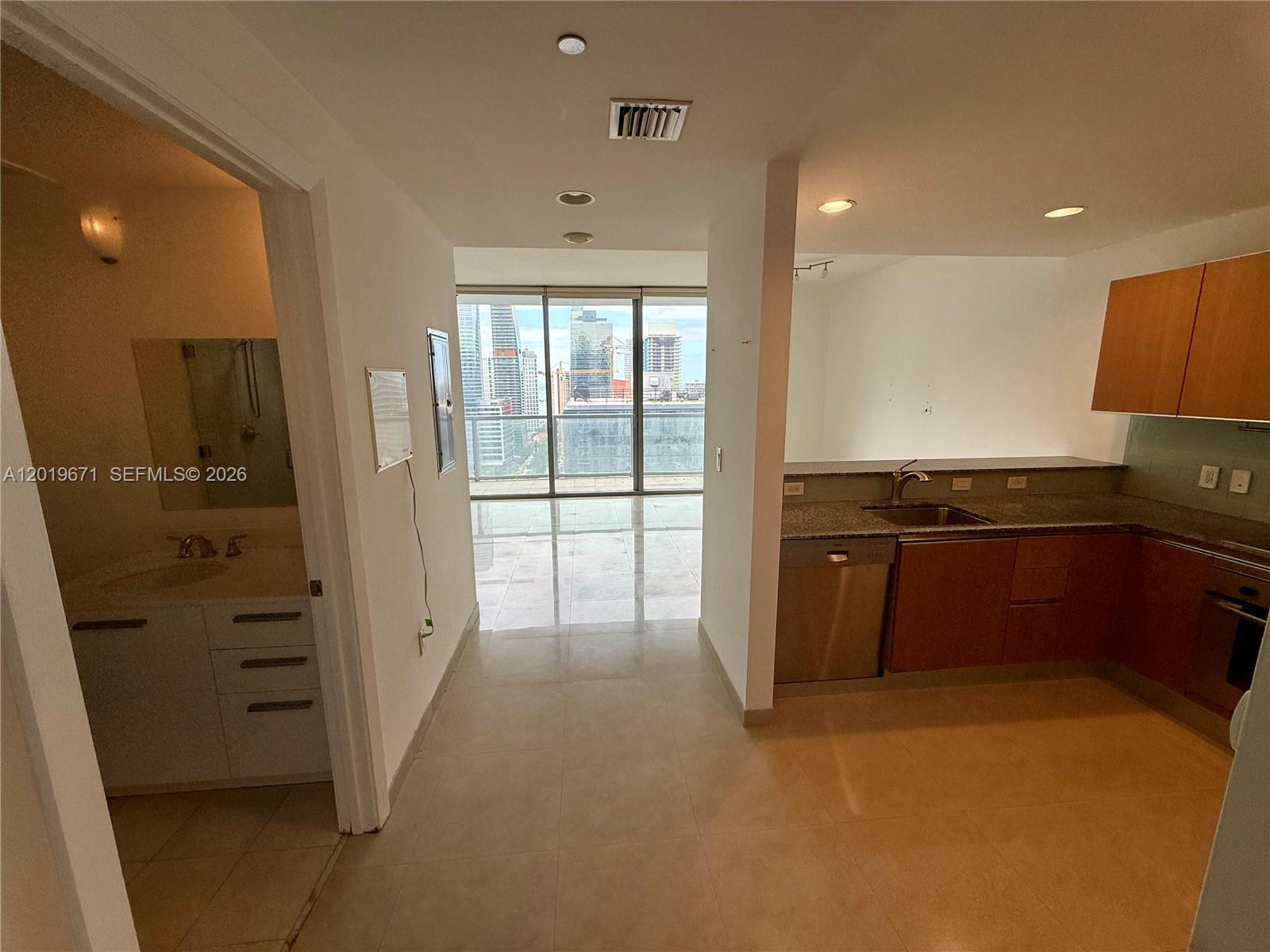 A kitchen with wood cabinets and stainless appliances sits adjacent to a bathroom and balcony — 1060 Brickell Ave # 2409, Miami FL 33131, MIAMI, FL