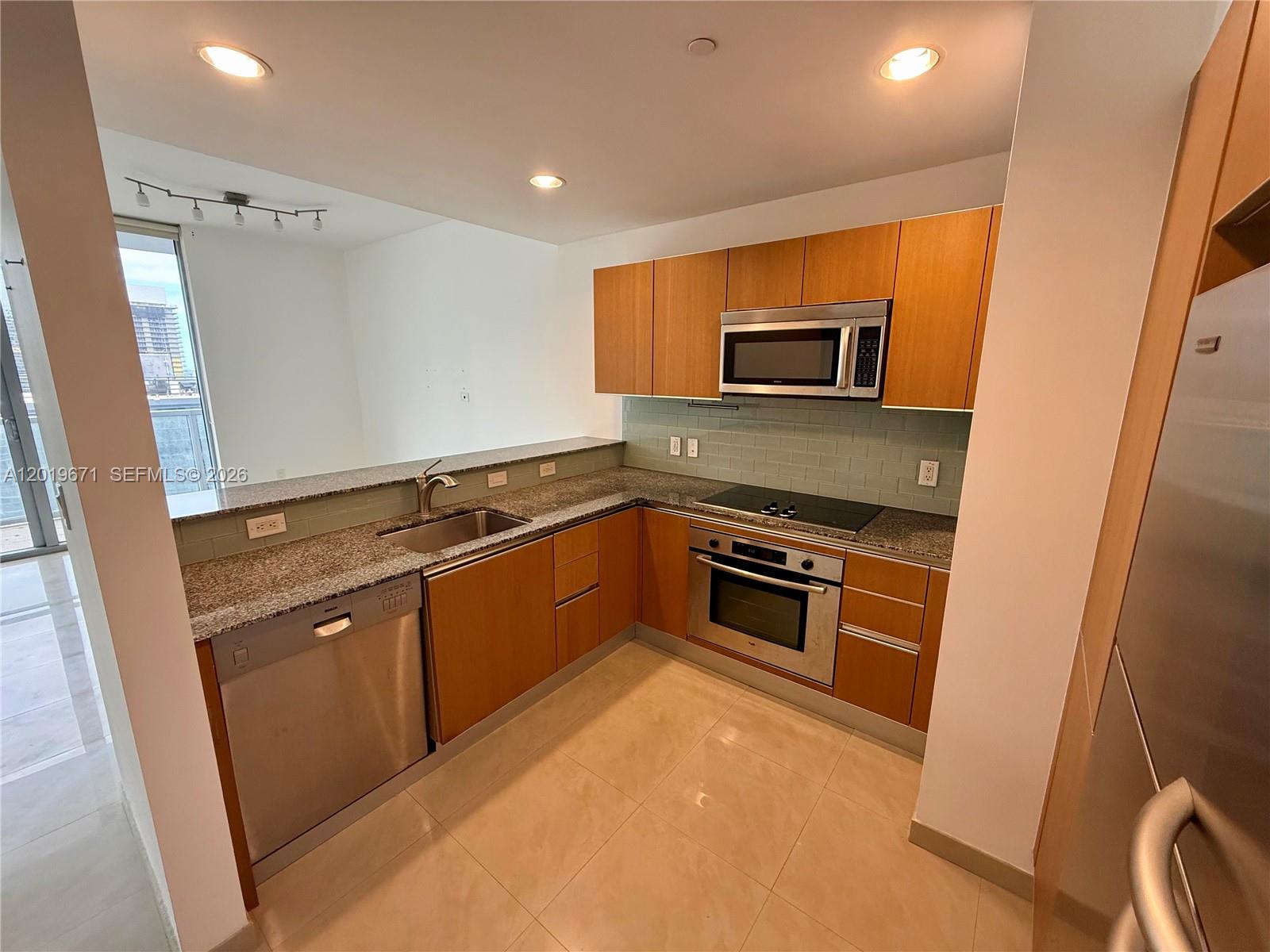 A kitchen features wood cabinets, granite countertops, stainless steel appliances, and a light tile floor — 1060 Brickell Ave # 2409, Miami FL 33131, MIAMI, FL