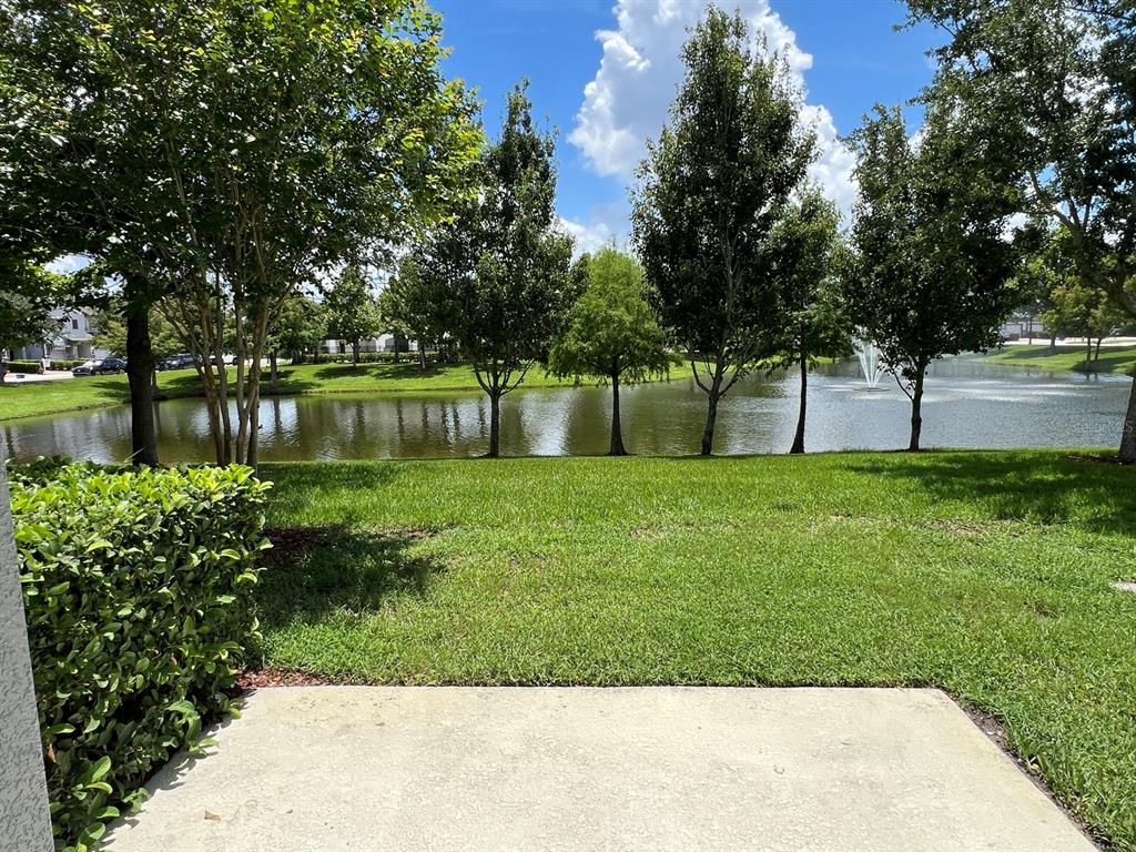 A concrete patio overlooks a grassy lawn, a pond with a fountain, and several trees — 321 EVERTREE LOOP, SANFORD, FL