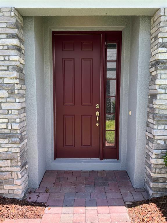 A red front door with a side window is flanked by stone pillars and pavers — 321 EVERTREE LOOP, SANFORD, FL