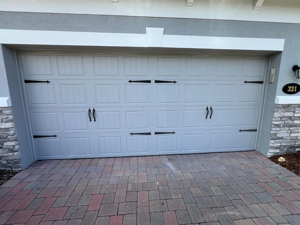 A light gray garage door with decorative black hardware is set in a stone-accented exterior — 321 EVERTREE LOOP, SANFORD, FL