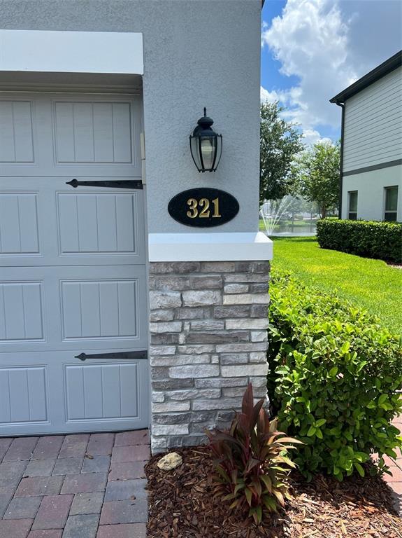 A gray garage door sits beside a stone-accented wall featuring a house number plaque — 321 EVERTREE LOOP, SANFORD, FL