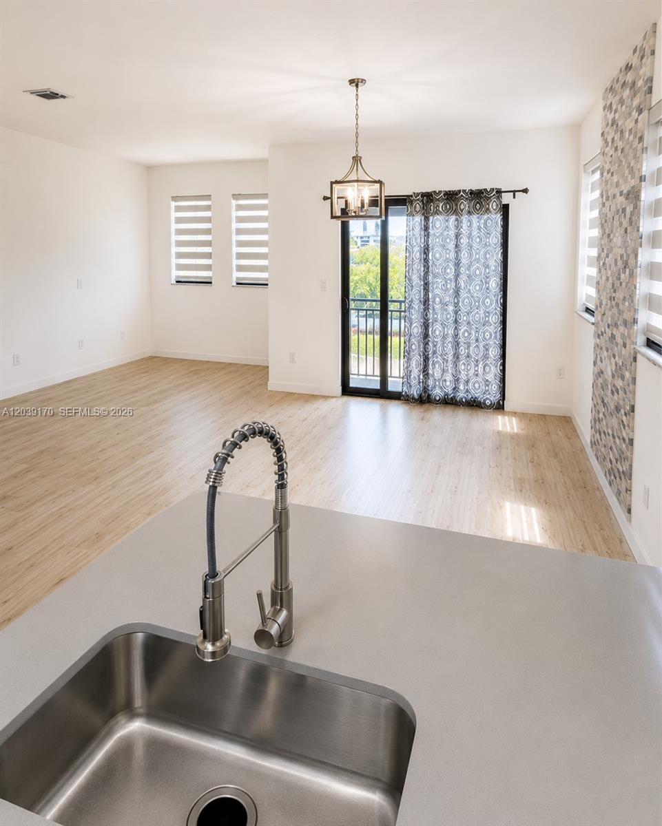 A kitchen sink overlooks an open-concept living area with light wood flooring and balcony access — 15560 SW 136th St # 201, Miami FL 33196, MIAMI, FL