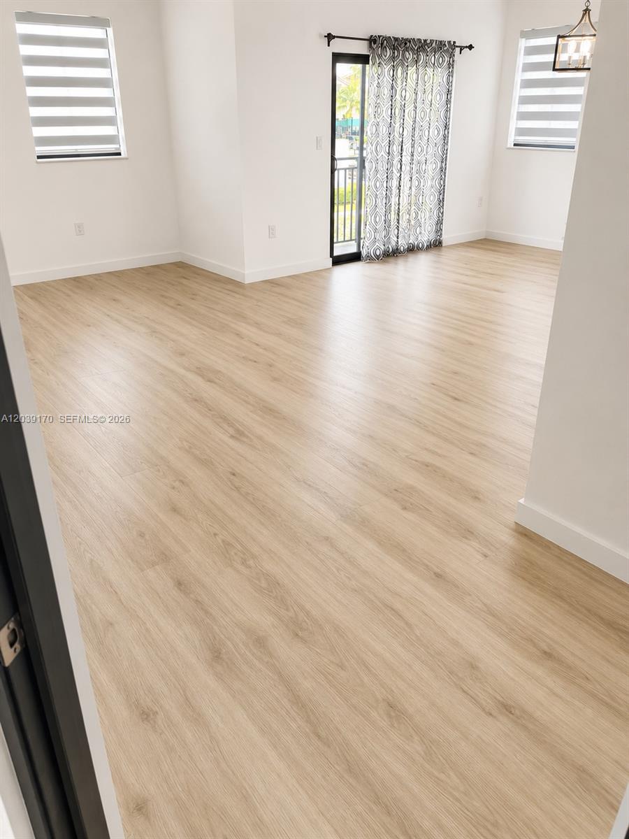 An empty room features light wood-look flooring, white walls, two windows with blinds, and a sliding glass door — 15560 SW 136th St # 201, Miami FL 33196, MIAMI, FL