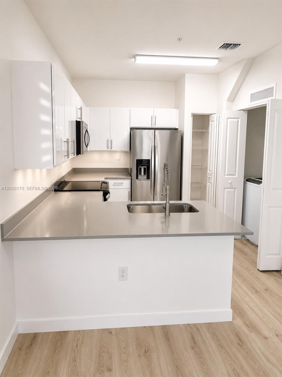 A modern kitchen features white cabinets, stainless steel appliances, and a gray countertop peninsula — 15560 SW 136th St # 201, Miami FL 33196, MIAMI, FL