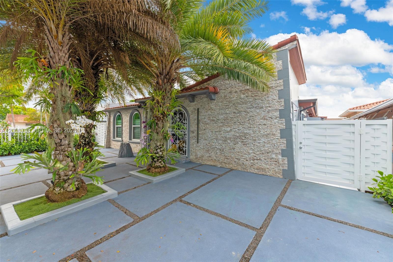 A stone-faced house exterior features a paved driveway, palm trees, and a white gate — 1870 NW 32nd Ave, Miami FL 33125, MIAMI, FL