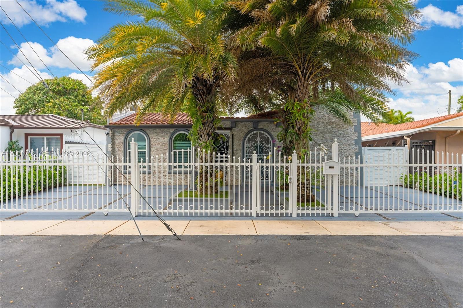A single-story house with a stone facade and palm trees behind a white metal fence — 1870 NW 32nd Ave, Miami FL 33125, MIAMI, FL