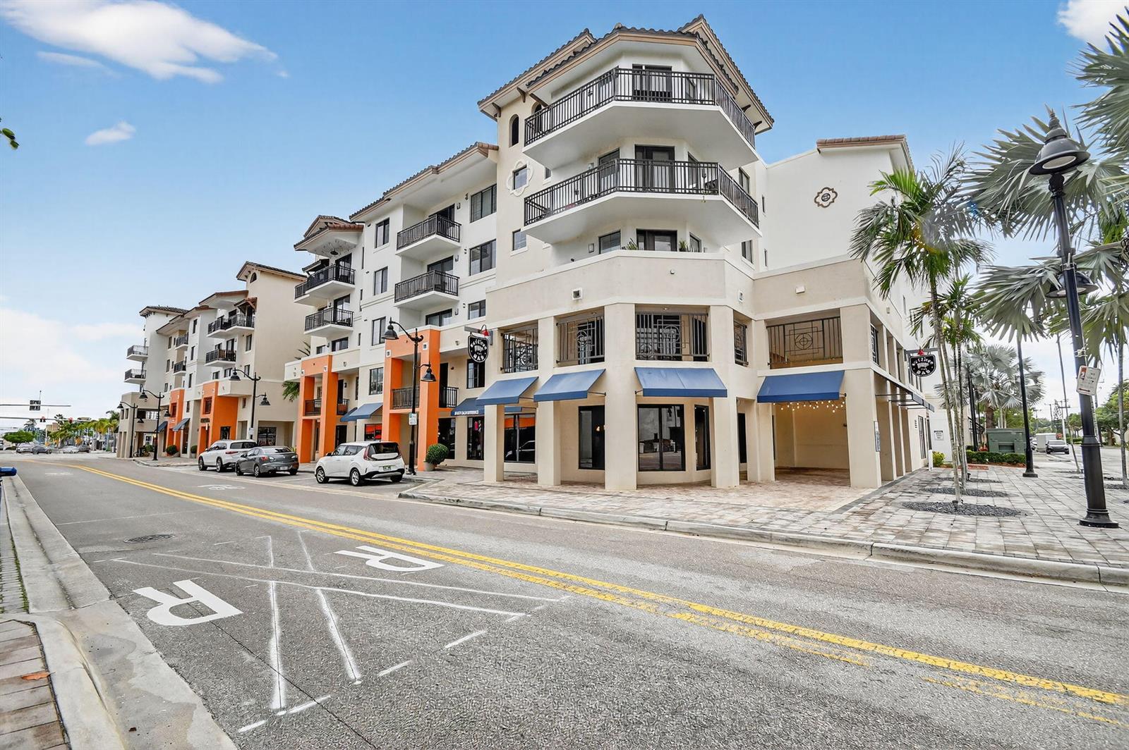 A multi-story building with balconies and ground-floor storefronts sits along a street with parking — 510 E Ocean Avenue # 102, Boynton Beach FL 33435, BOYNTON BEACH, FL