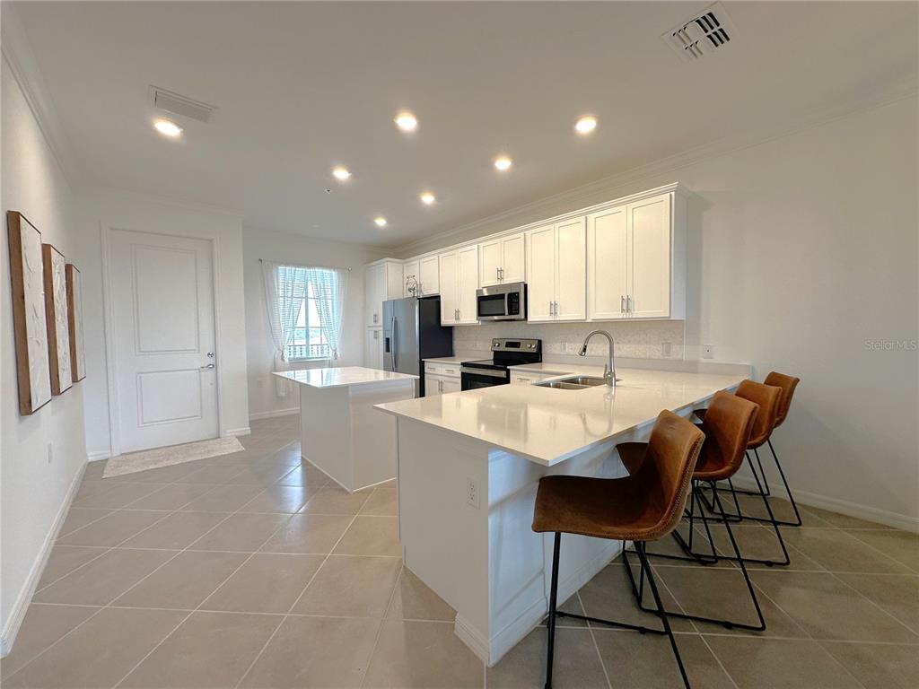 A modern kitchen features white cabinetry, stainless steel appliances, a center island, and tile flooring — 14121 HERITAGE LANDING BOULEVARD UNIT 743, PUNTA GORDA, FL