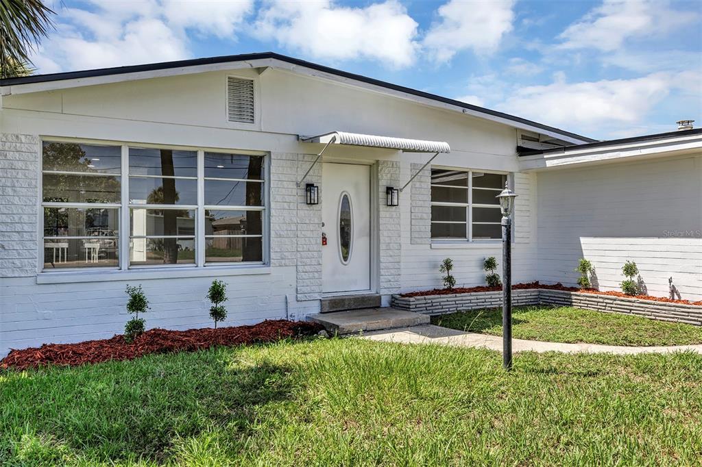 The exterior of a white brick house features a front door with a metal awning — 332 WILLIAMS AVENUE, DAYTONA BEACH, FL