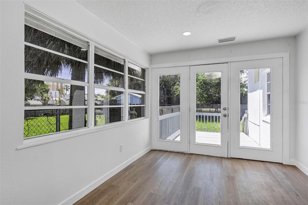 A sunroom with white walls, wood-look flooring, large windows, and glass doors leading to a deck — 332 WILLIAMS AVENUE, DAYTONA BEACH, FL