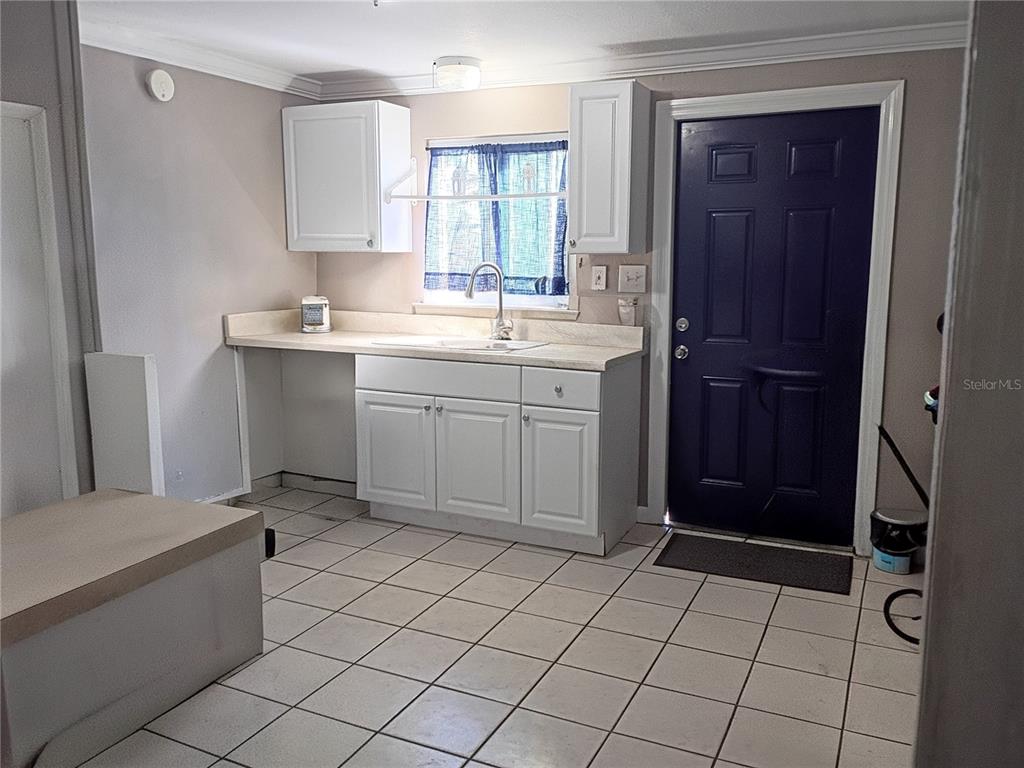 A kitchen features white cabinets, a sink, tiled flooring, and a dark blue exterior door — 2601 MANATEE HARBOR DRIVE, RUSKIN, FL