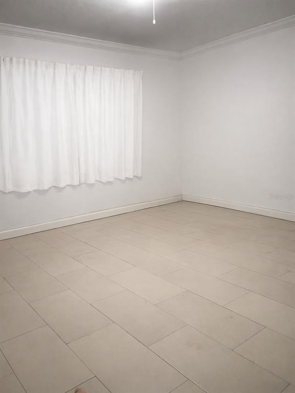 An empty room features white walls, crown molding, white curtains, and light-colored tile flooring — 2601 MANATEE HARBOR DRIVE, RUSKIN, FL