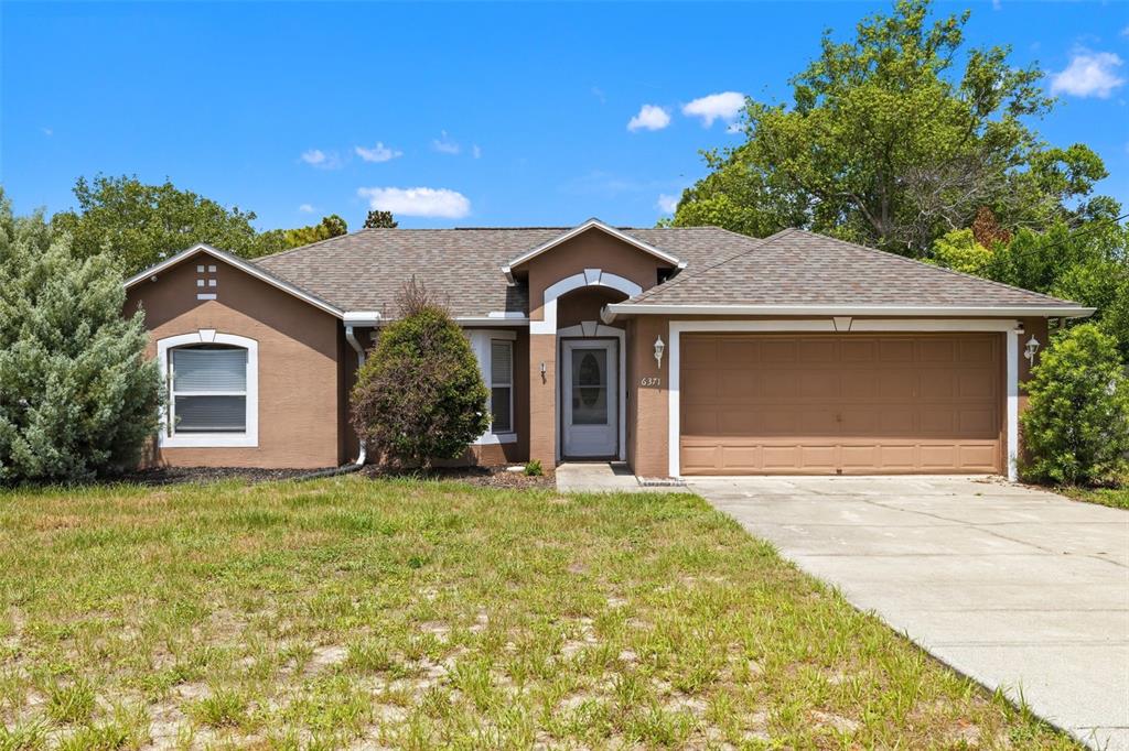 A single-story house with brown stucco siding, a two-car garage, and a concrete driveway — 6371 SHADYDALE AVENUE, SPRING HILL, FL