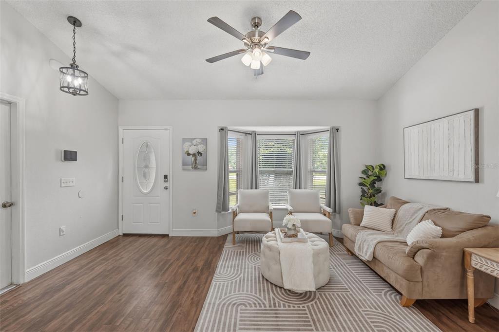 A living room features wood-look flooring, a bay window, a ceiling fan, and neutral furniture — 6371 SHADYDALE AVENUE, SPRING HILL, FL