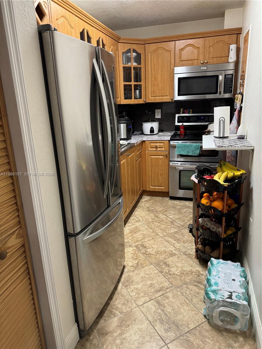 A galley kitchen features wood cabinets, stainless steel appliances, and beige tile flooring — 4717 NW 7th St # 10, Miami FL 33126, MIAMI, FL