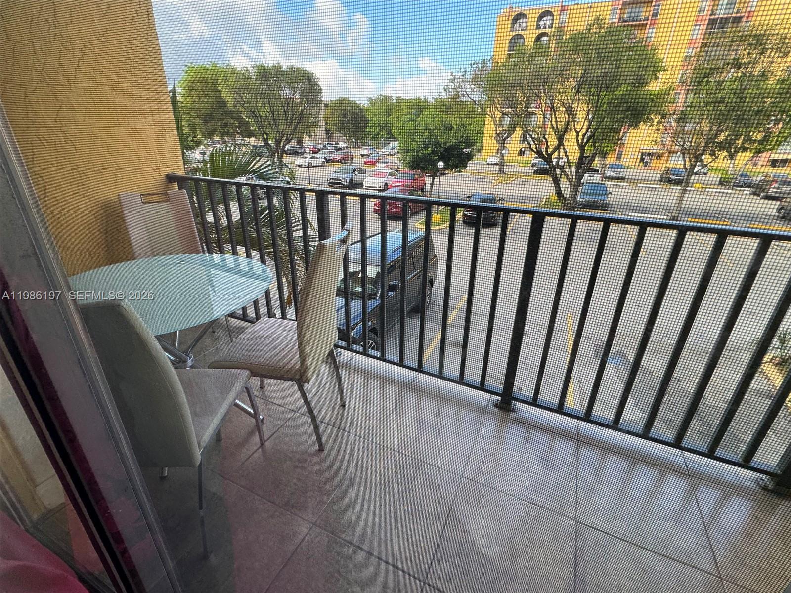 A balcony features a glass-topped table, two chairs, and a metal railing overlooking a parking lot — 4717 NW 7th St # 10, Miami FL 33126, MIAMI, FL