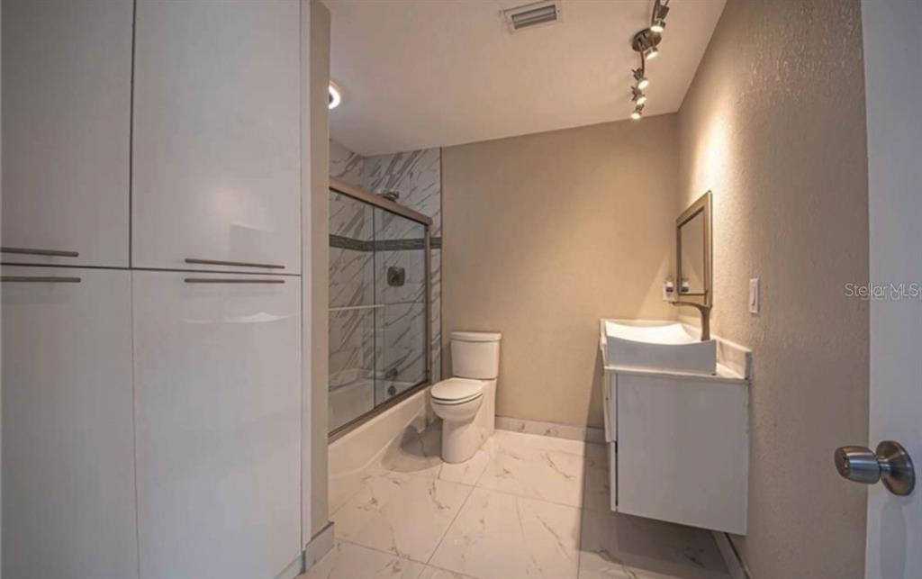 A bathroom features white cabinets, a glass-enclosed shower, a toilet, and light-colored marble-look tile flooring — 2516 BALTIC AVENUE, PORT CHARLOTTE, FL