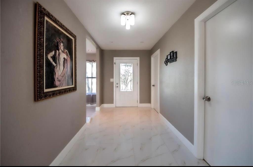 A bright entryway features light gray walls, white trim, marble-look tile flooring, and a front door — 2516 BALTIC AVENUE, PORT CHARLOTTE, FL