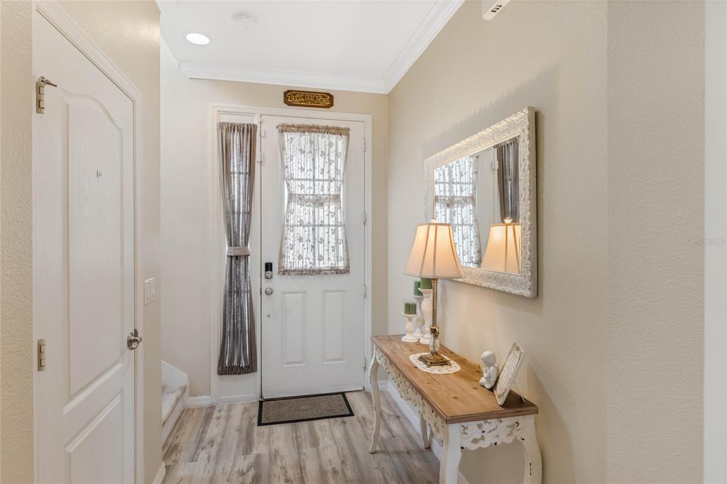 An entryway features a white front door, a wood console table, and a wall mirror — 1411 PACIFIC ROAD, POINCIANA, FL