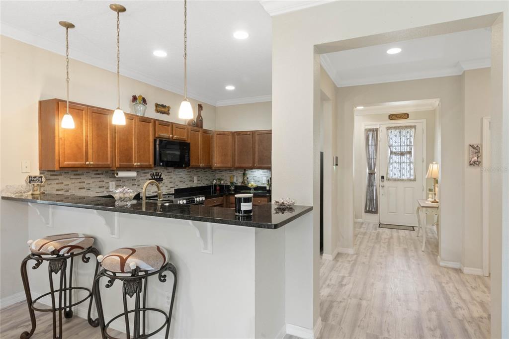 A kitchen with wood cabinets and dark countertops overlooks a hallway with a front door — 1411 PACIFIC ROAD, POINCIANA, FL