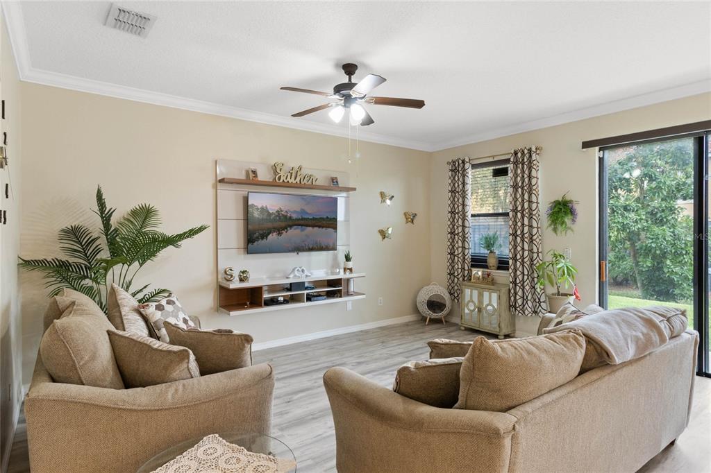 A living room features a wall-mounted television, beige sofas, and a ceiling fan — 1411 PACIFIC ROAD, POINCIANA, FL