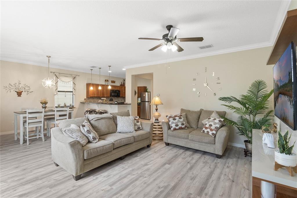 A living room with light wood-look flooring, beige walls, a ceiling fan, and open kitchen — 1411 PACIFIC ROAD, POINCIANA, FL