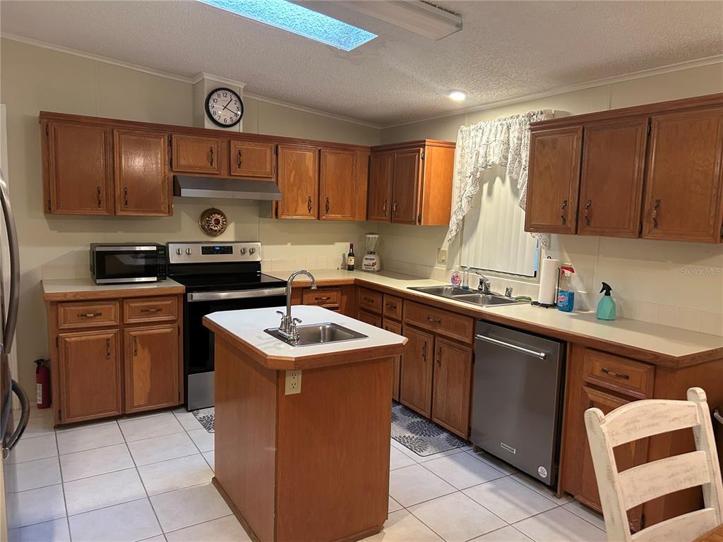 A kitchen features wood cabinets, a central island with a sink, and stainless steel appliances — 252 RITA BEE AVENUE, DAVENPORT, FL