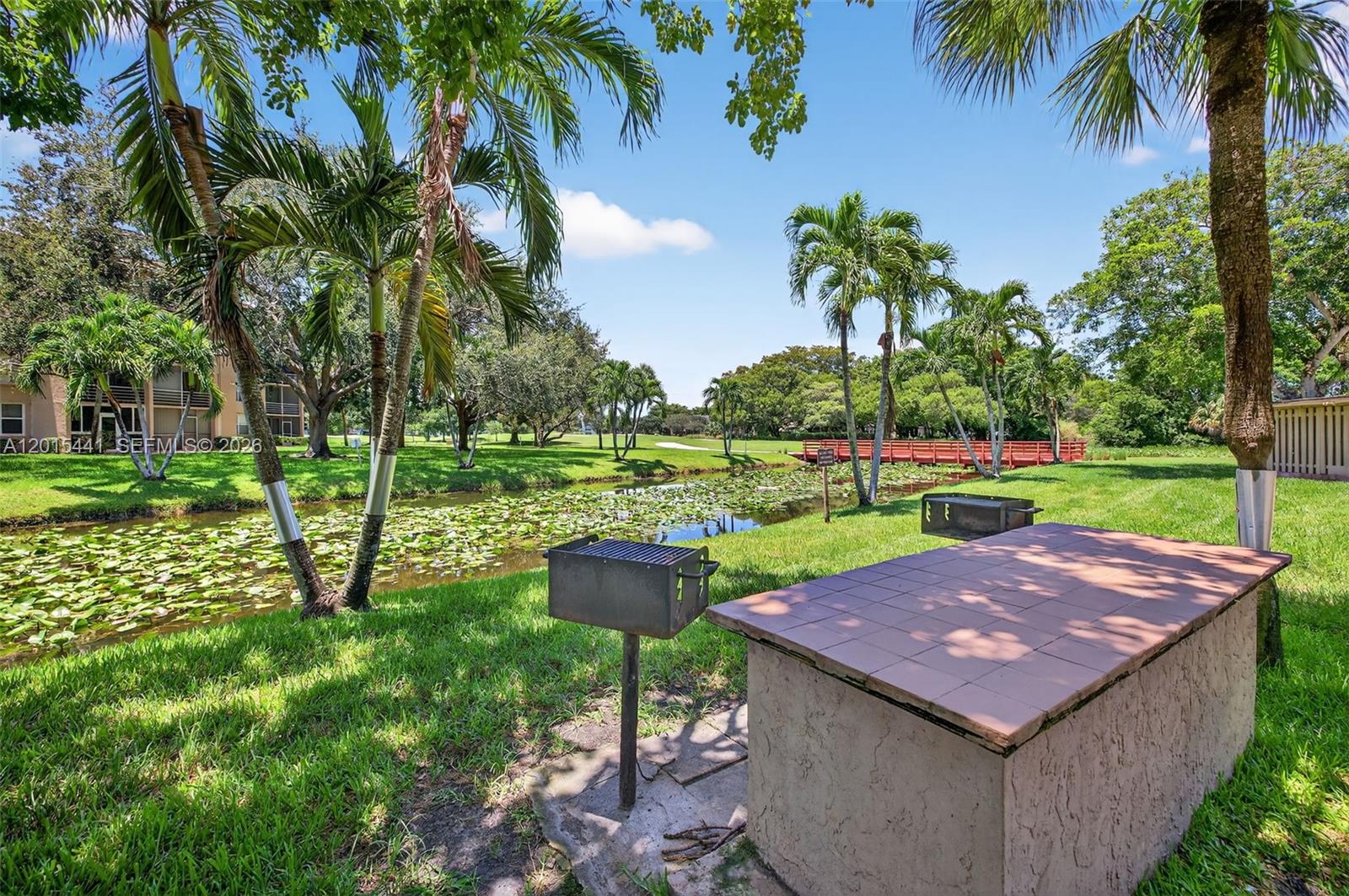 A grassy park area features a brick grill, a tile-topped table, and a lily-covered pond — 9470 Tangerine Pl # 105, Davie FL 33324, DAVIE, FL
