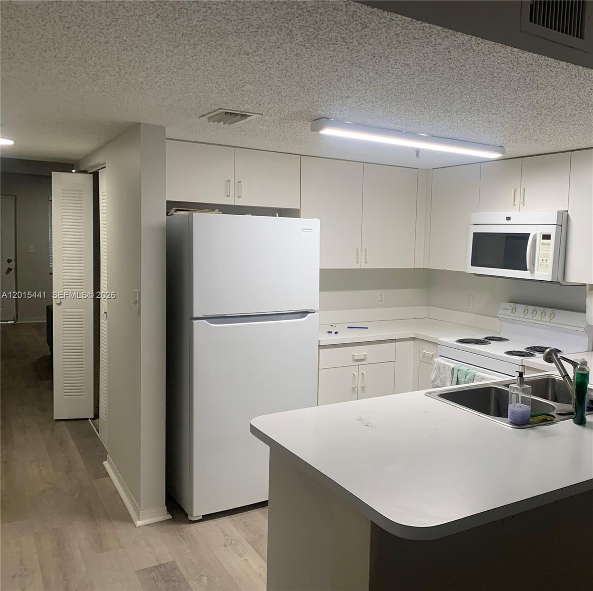 A kitchen features white cabinetry, white appliances, a peninsula countertop, and light-colored wood flooring — 9470 Tangerine Pl # 105, Davie FL 33324, DAVIE, FL