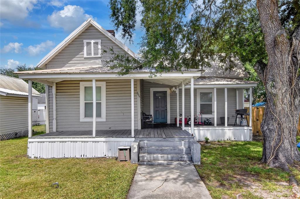 A gray, single-story house with a front porch, metal roof, and a large tree — 204 NE 1ST AVENUE, MULBERRY, FL