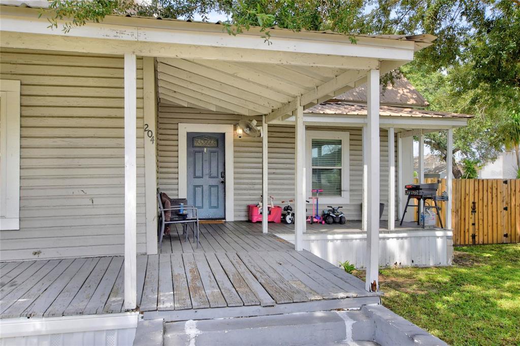 A weathered wooden porch leads to a blue front door on a light-colored house — 204 NE 1ST AVENUE, MULBERRY, FL