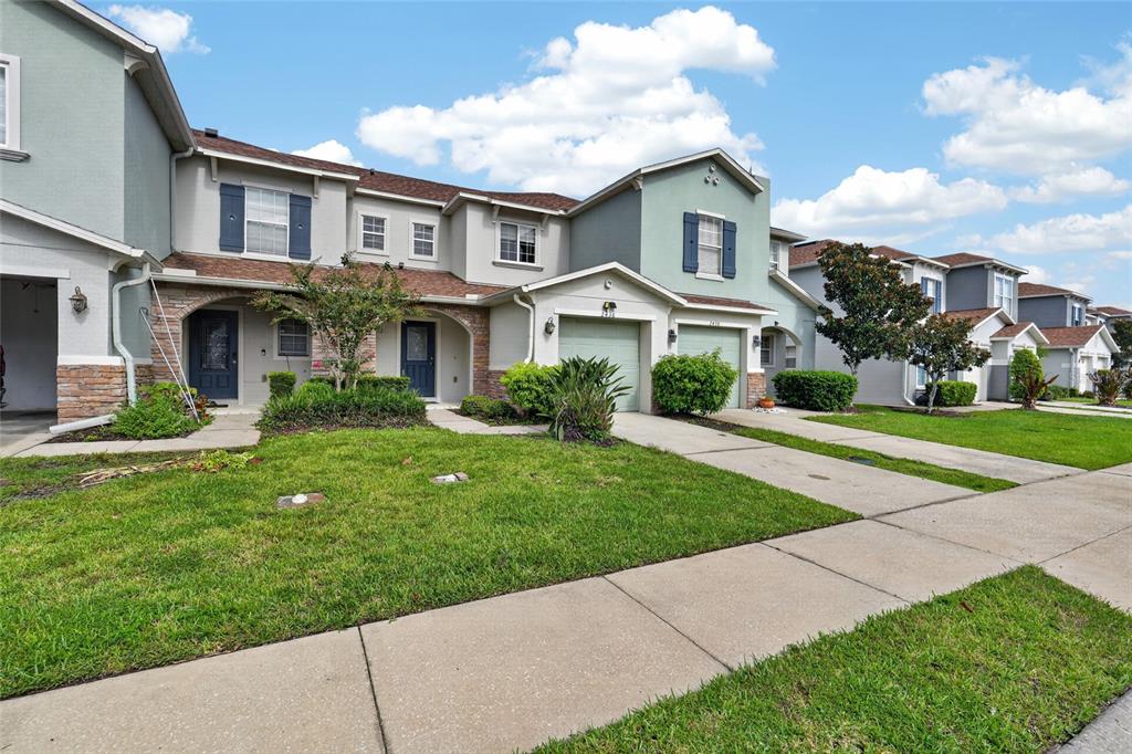 A row of multi-story townhomes features stone accents, attached garages, and manicured front lawns — 2436 HASSONITE STREET, KISSIMMEE, FL