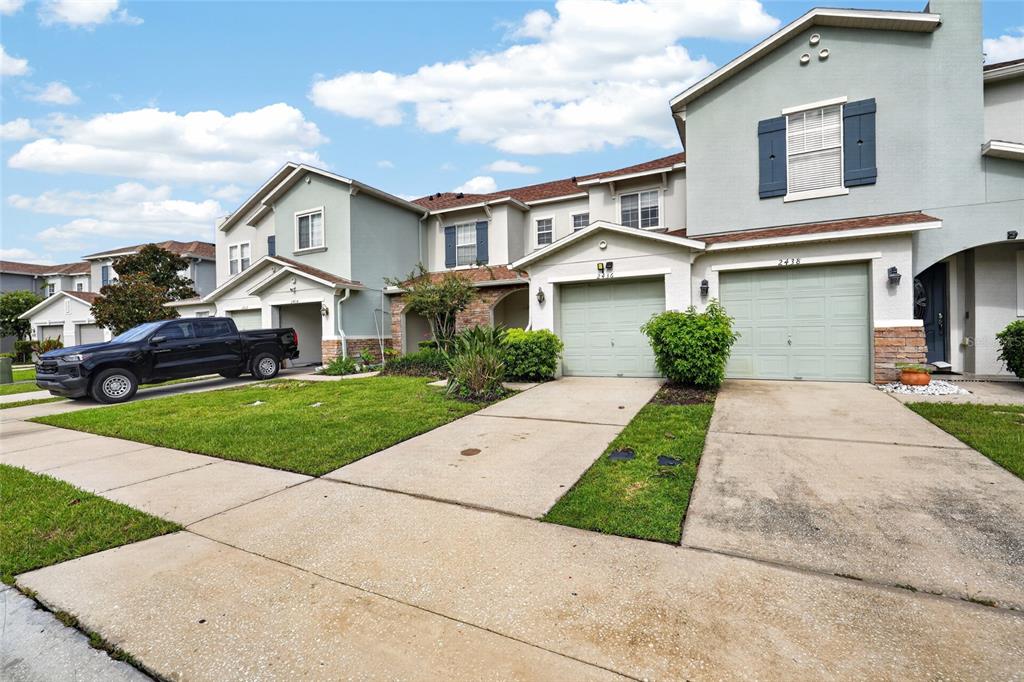 A row of two-story townhomes with light-colored stucco, attached garages, and a parked pickup truck — 2436 HASSONITE STREET, KISSIMMEE, FL