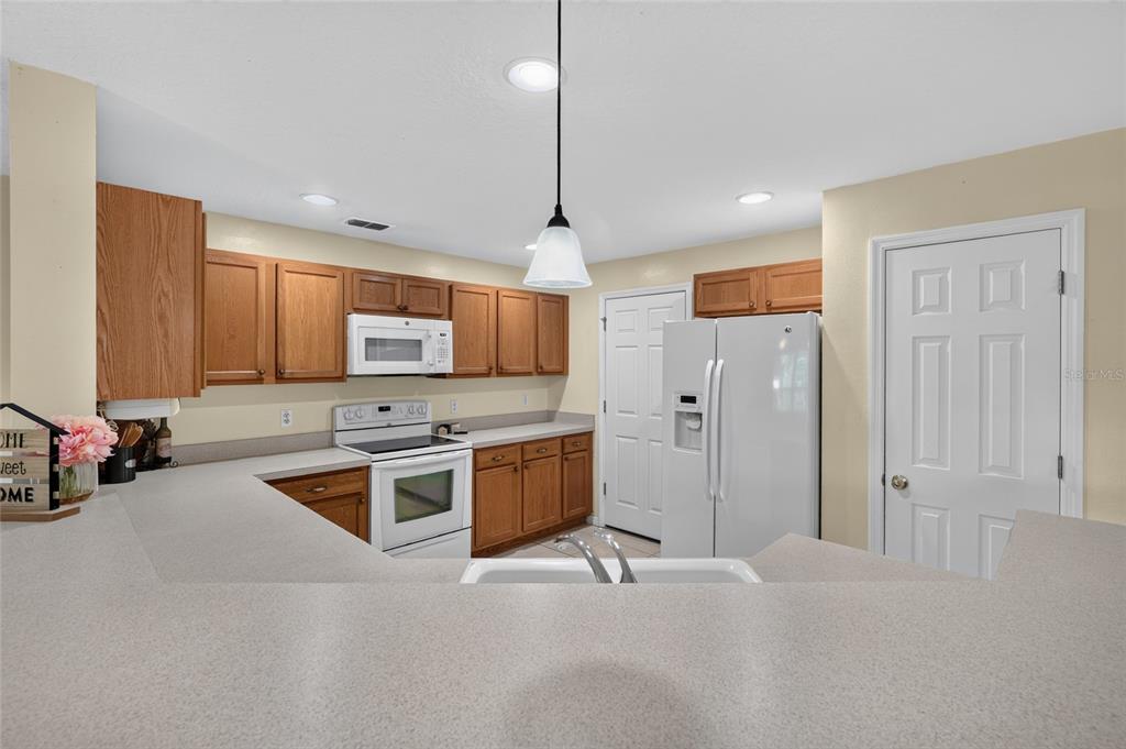 A kitchen features wood cabinets, white appliances, and a peninsula countertop with a sink — 2436 HASSONITE STREET, KISSIMMEE, FL