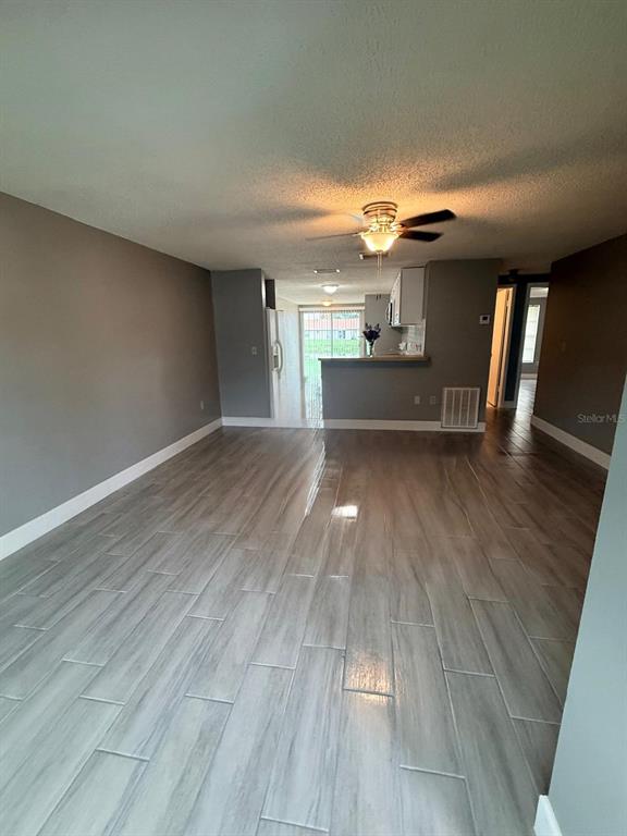 A living room with light wood-look tile flooring leads to an open kitchen and patio — 4212 78TH STREET W UNIT 4212, BRADENTON, FL